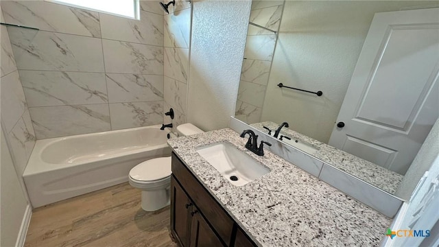 full bathroom featuring washtub / shower combination, wood finished floors, toilet, vanity, and a textured wall