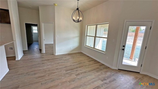 unfurnished dining area with an inviting chandelier, vaulted ceiling, baseboards, and light wood finished floors