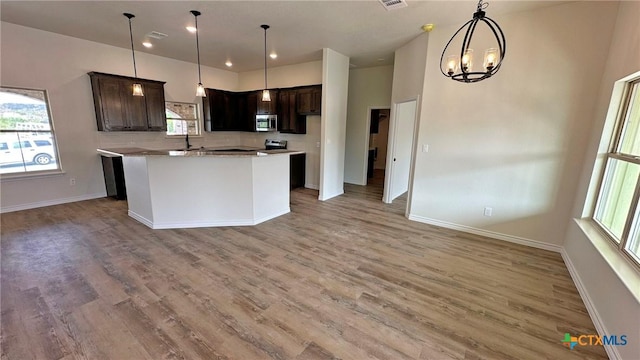 kitchen featuring dark brown cabinets, a notable chandelier, light wood-style floors, and stainless steel microwave