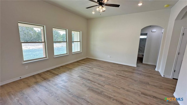unfurnished room with baseboards, wood finished floors, arched walkways, and a ceiling fan