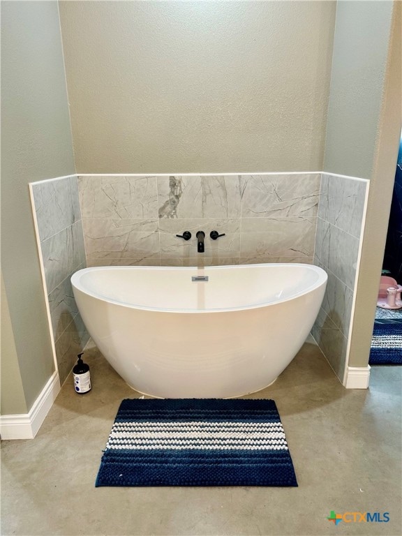 bathroom with concrete flooring, tile walls, and a bathing tub