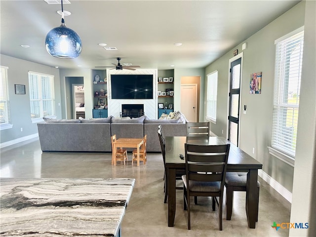 dining room with a fireplace, built in features, a healthy amount of sunlight, and concrete floors