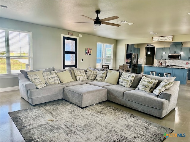 living room featuring concrete flooring, sink, ceiling fan, and a textured ceiling