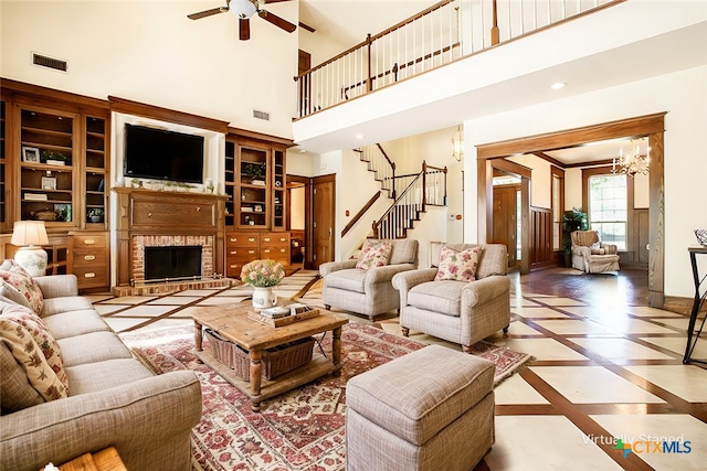 living room with a fireplace, a high ceiling, and ceiling fan with notable chandelier