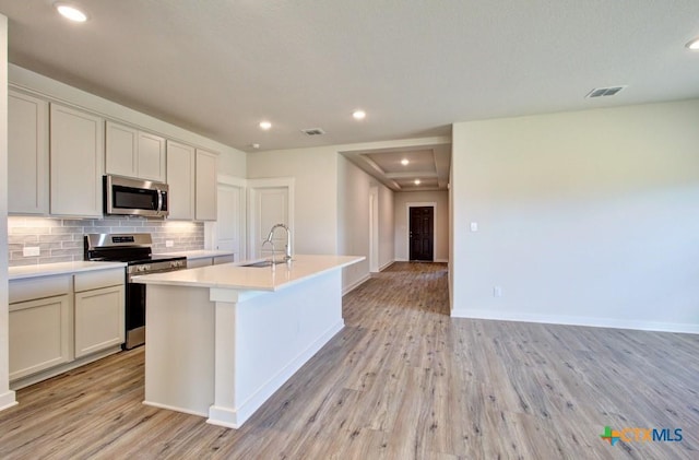 911 Cloud Sky Rd, New Braunfels, TX 78130 - kitchen with appliances with stainless steel finishes, light wood-type flooring, a kitchen island with sink, light countertops, and backsplash