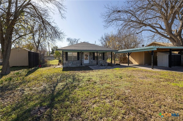 rear view of property featuring a lawn, a carport, and a storage unit