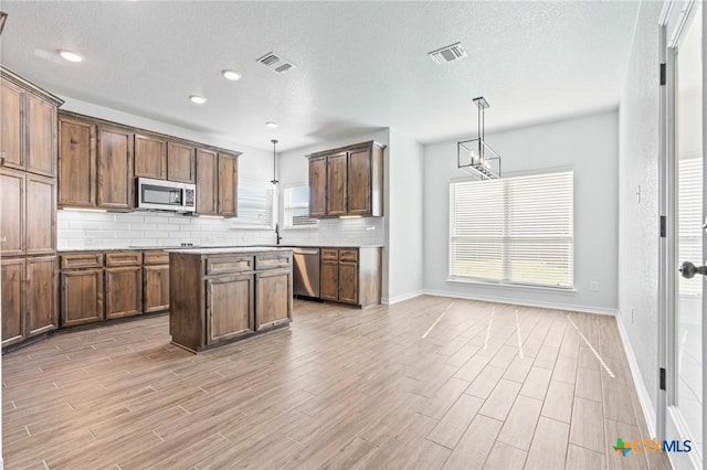 kitchen with pendant lighting, backsplash, a textured ceiling, a kitchen island, and stainless steel appliances