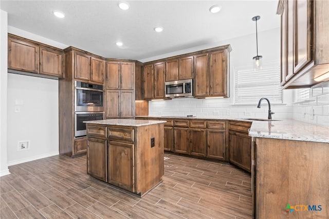 kitchen featuring light stone countertops, sink, stainless steel appliances, decorative light fixtures, and a kitchen island