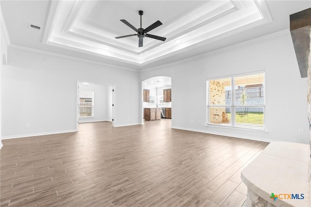 unfurnished living room featuring a tray ceiling, ceiling fan, and ornamental molding