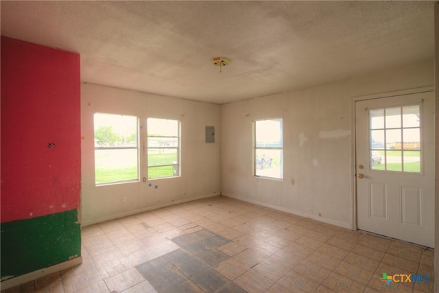 empty room featuring a textured ceiling, electric panel, and a wealth of natural light