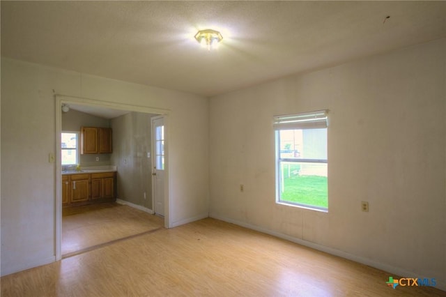 empty room with sink, lofted ceiling, and light wood-type flooring