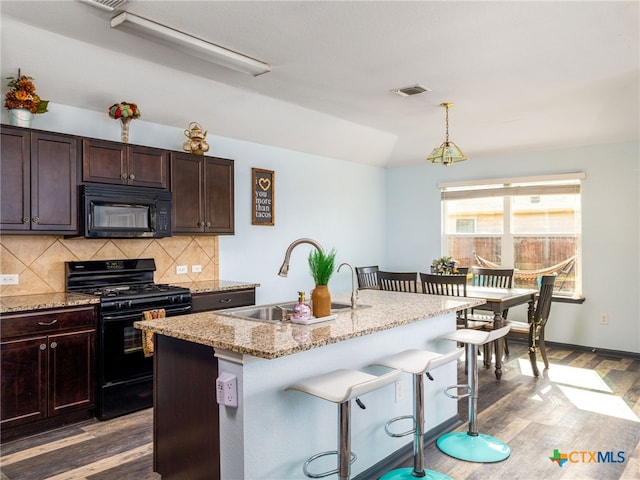 900 Hatton Hill Ln, Austin, TX 78725 - kitchen featuring black appliances, a breakfast bar, wood finished floors, decorative backsplash, and light stone counters