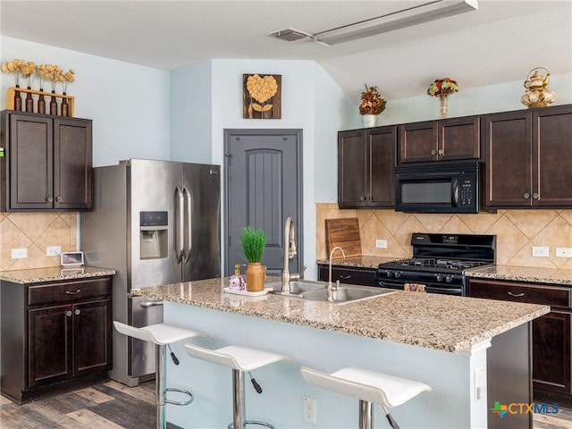 900 Hatton Hill Ln, Austin, TX 78725 - kitchen featuring black appliances, dark brown cabinets, lofted ceiling, a breakfast bar, and light wood-style flooring