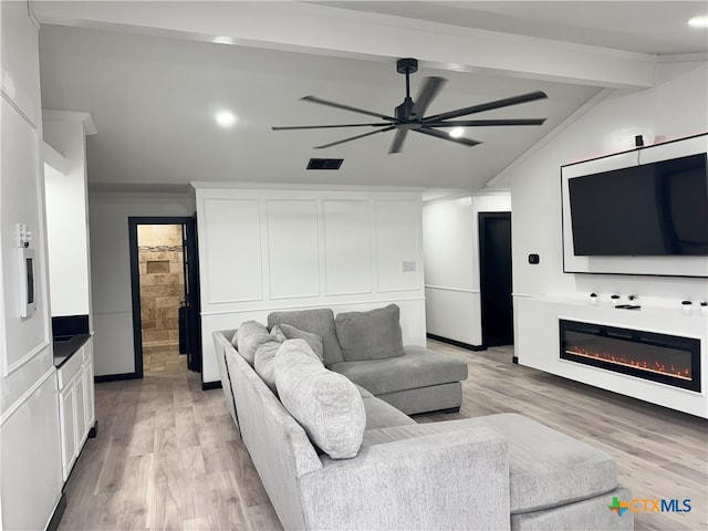 living area with light wood finished floors, vaulted ceiling with beams, a glass covered fireplace, visible vents, and ceiling fan