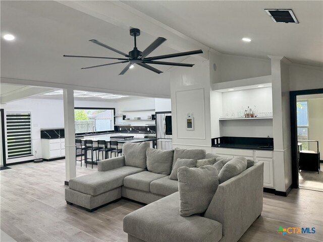 living area with lofted ceiling with beams, visible vents, bar, a ceiling fan, and light wood-type flooring