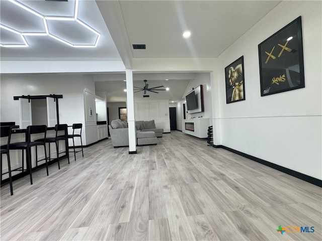 living area featuring baseboards, a barn door, visible vents, a ceiling fan, and wood finished floors