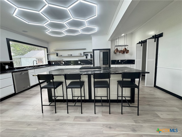 kitchen featuring open shelves, white cabinetry, a barn door, stainless steel appliances, and dark countertops