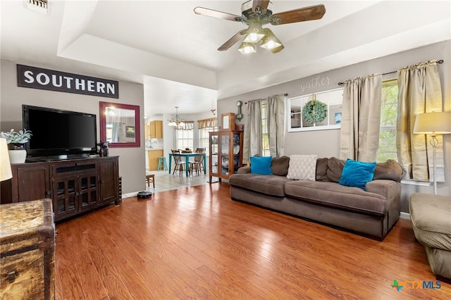 living area featuring a tray ceiling, wood finished floors, visible vents, and ceiling fan with notable chandelier