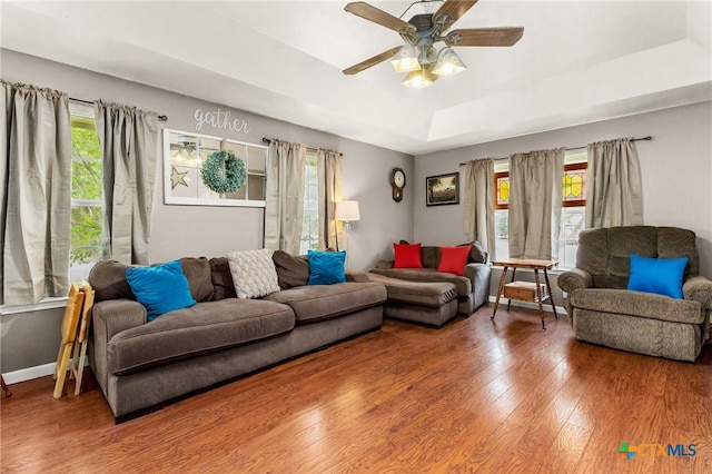 living area with a raised ceiling, wood finished floors, and ceiling fan