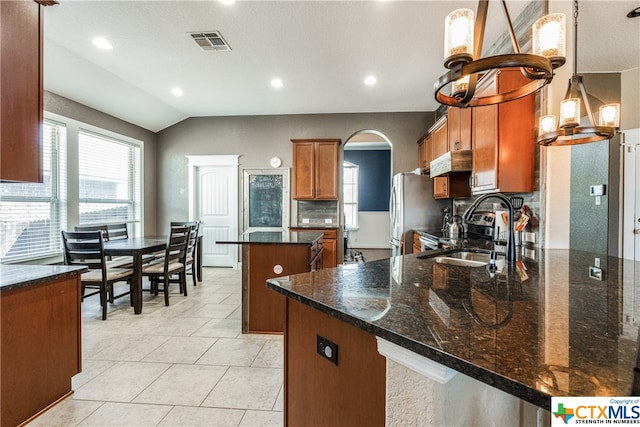 kitchen with vaulted ceiling, sink, backsplash, decorative light fixtures, and dark stone countertops