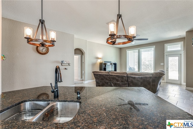 kitchen with sink, ceiling fan, dark stone countertops, a textured ceiling, and decorative light fixtures