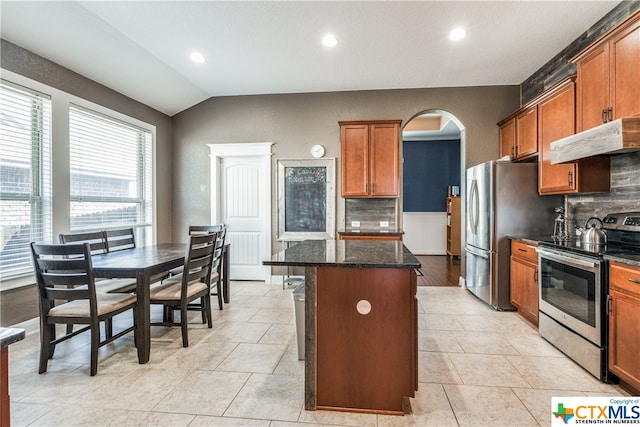 kitchen with backsplash, appliances with stainless steel finishes, vaulted ceiling, dark stone countertops, and a center island