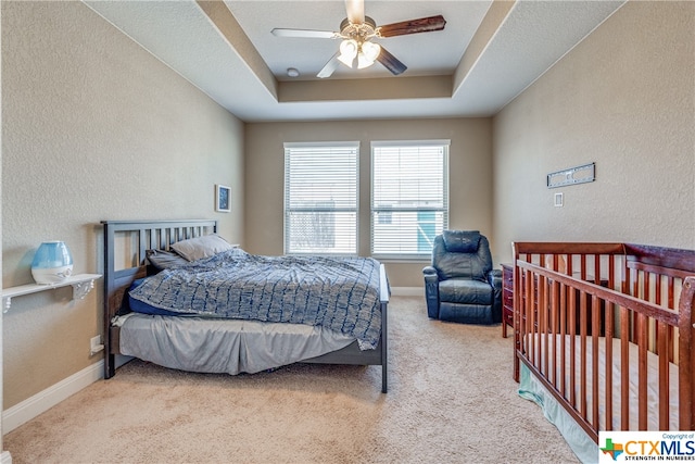 carpeted bedroom featuring ceiling fan and a raised ceiling