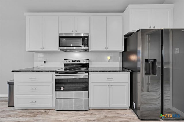 kitchen with appliances with stainless steel finishes, dark stone countertops, and white cabinetry