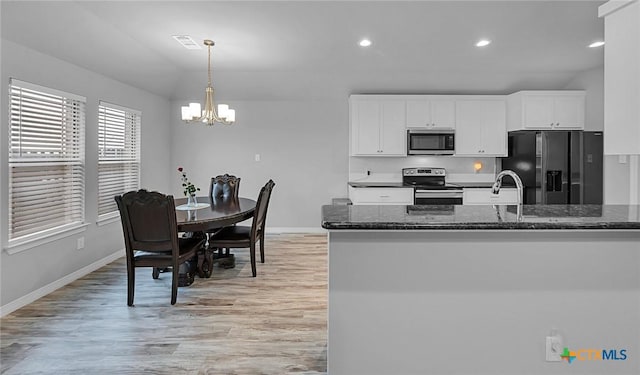 kitchen with white cabinetry, light hardwood / wood-style floors, stainless steel appliances, decorative light fixtures, and dark stone counters