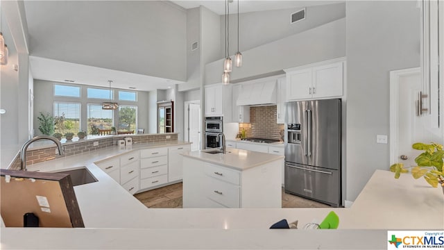 kitchen with stainless steel appliances, sink, a kitchen island, backsplash, and a high ceiling