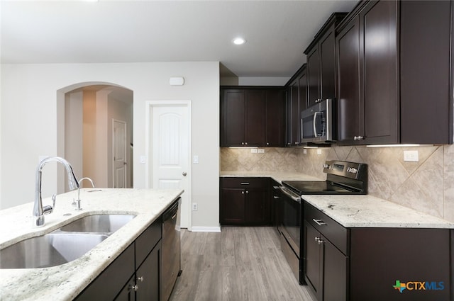 kitchen with sink, light stone countertops, light wood-type flooring, appliances with stainless steel finishes, and tasteful backsplash