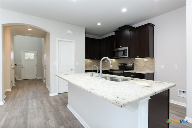 kitchen featuring a center island with sink, sink, appliances with stainless steel finishes, light hardwood / wood-style floors, and light stone counters