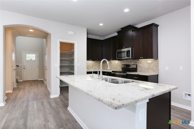 kitchen with a center island with sink, light stone countertops, light wood-type flooring, and stainless steel appliances