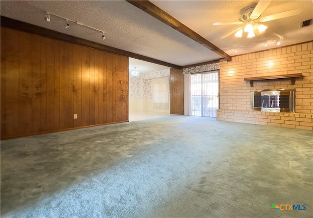 unfurnished living room with beam ceiling, a textured ceiling, wooden walls, and a brick fireplace