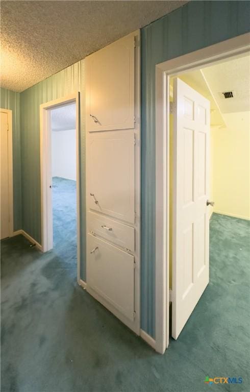 hall featuring a textured ceiling and dark colored carpet