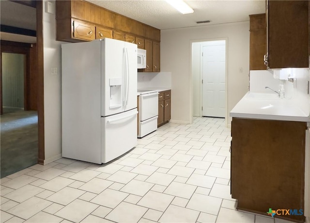 kitchen featuring a textured ceiling, sink, light tile patterned floors, and white appliances