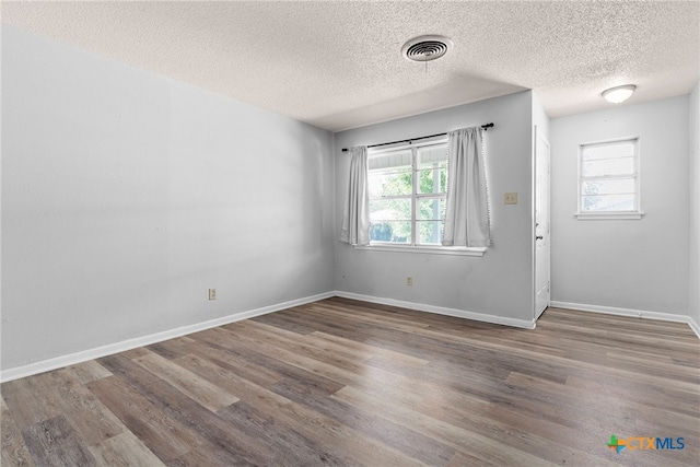 empty room with a textured ceiling, wood-type flooring, and plenty of natural light