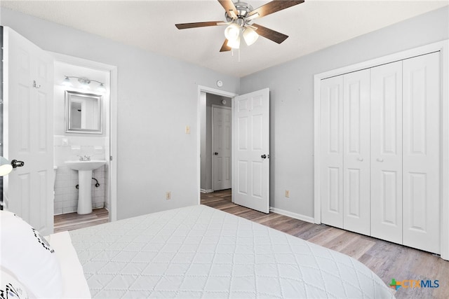 bedroom featuring tile walls, connected bathroom, light wood-type flooring, sink, and ceiling fan