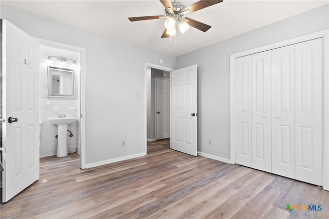 unfurnished bedroom with tile walls, ensuite bath, light wood-type flooring, sink, and ceiling fan