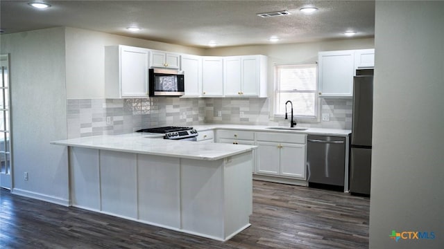 kitchen with kitchen peninsula, appliances with stainless steel finishes, sink, white cabinets, and dark hardwood / wood-style floors