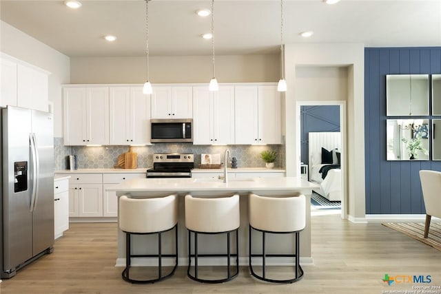 kitchen with appliances with stainless steel finishes, decorative light fixtures, white cabinetry, sink, and a kitchen island with sink