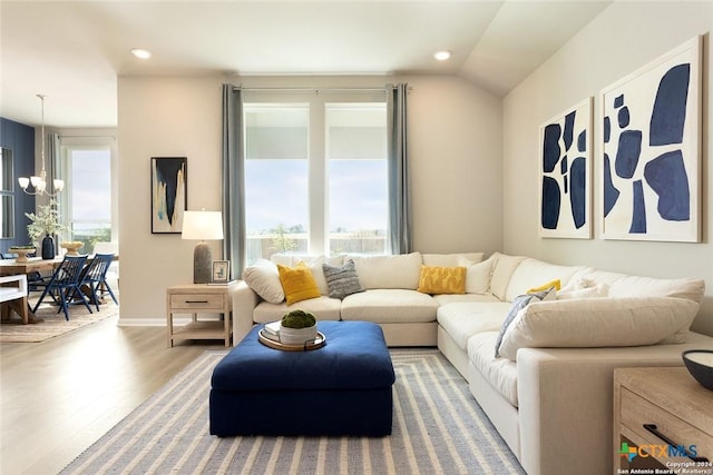 living room with lofted ceiling, a healthy amount of sunlight, hardwood / wood-style floors, and a notable chandelier