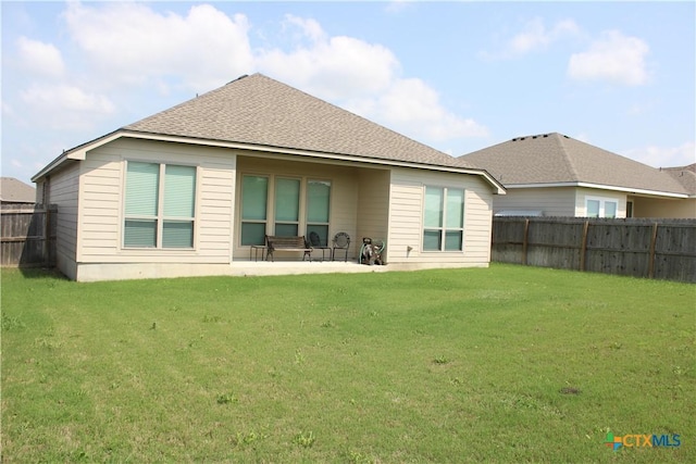 rear view of house with a fenced backyard, a shingled roof, and a lawn