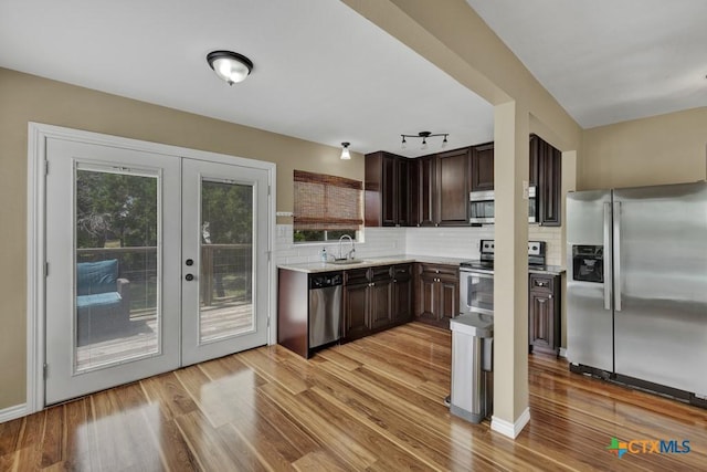1568 Blueridge Dr, Canyon Lake, TX 78133 - kitchen with stainless steel appliances, dark brown cabinetry, french doors, decorative backsplash, and light wood-style flooring