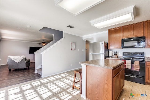 kitchen with light hardwood / wood-style floors, black appliances, ceiling fan, crown molding, and a center island