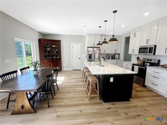 701 S Hudson St, Flatonia, TX 78941 - kitchen with appliances with stainless steel finishes, light countertops, a center island with sink, light wood-type flooring, and white cabinets