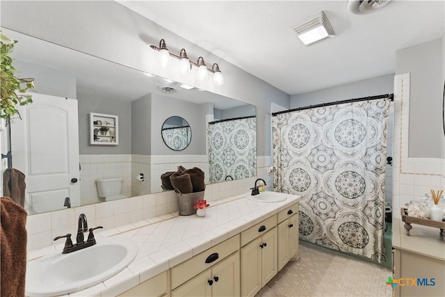 full bathroom featuring tile walls, a sink, and visible vents