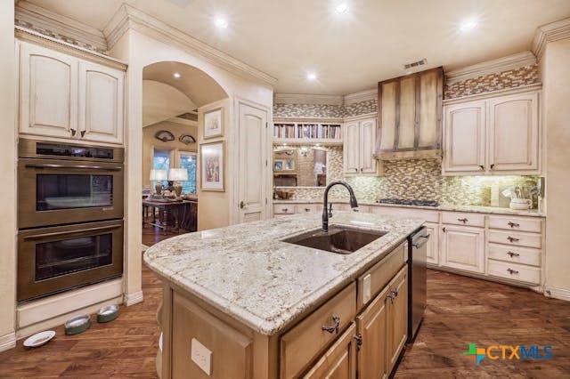 kitchen featuring a center island with sink, wall chimney range hood, appliances with stainless steel finishes, dark hardwood / wood-style floors, and sink