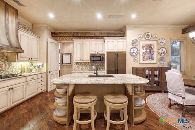 kitchen with light stone counters, appliances with stainless steel finishes, dark hardwood / wood-style floors, sink, and a kitchen island with sink