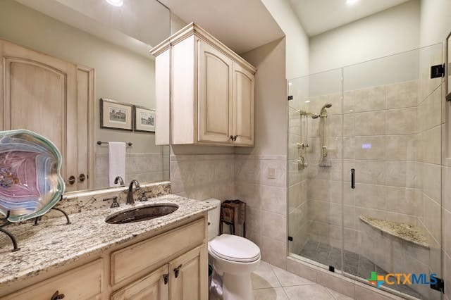 bathroom with tile patterned floors, toilet, tile walls, vanity, and walk in shower